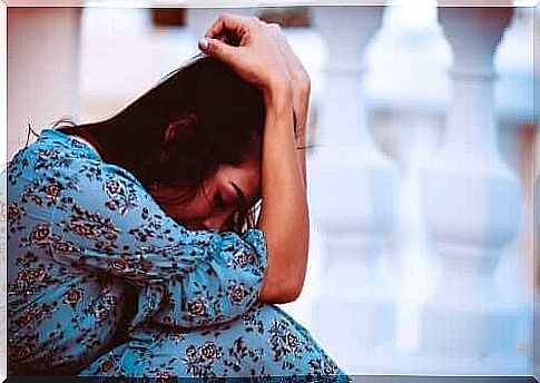 Woman in a blue, long dress hides her face in her hands.